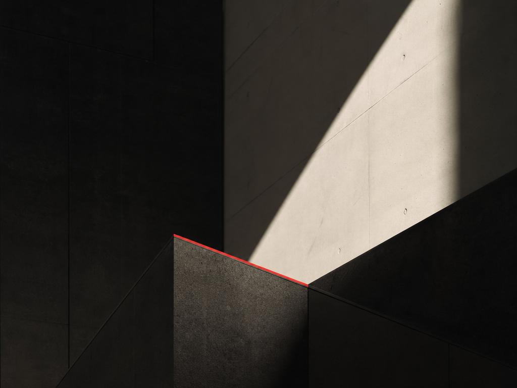 Minimalist architectural concrete and dark stone forms with elegant signal red accents and hard diagonal shadows